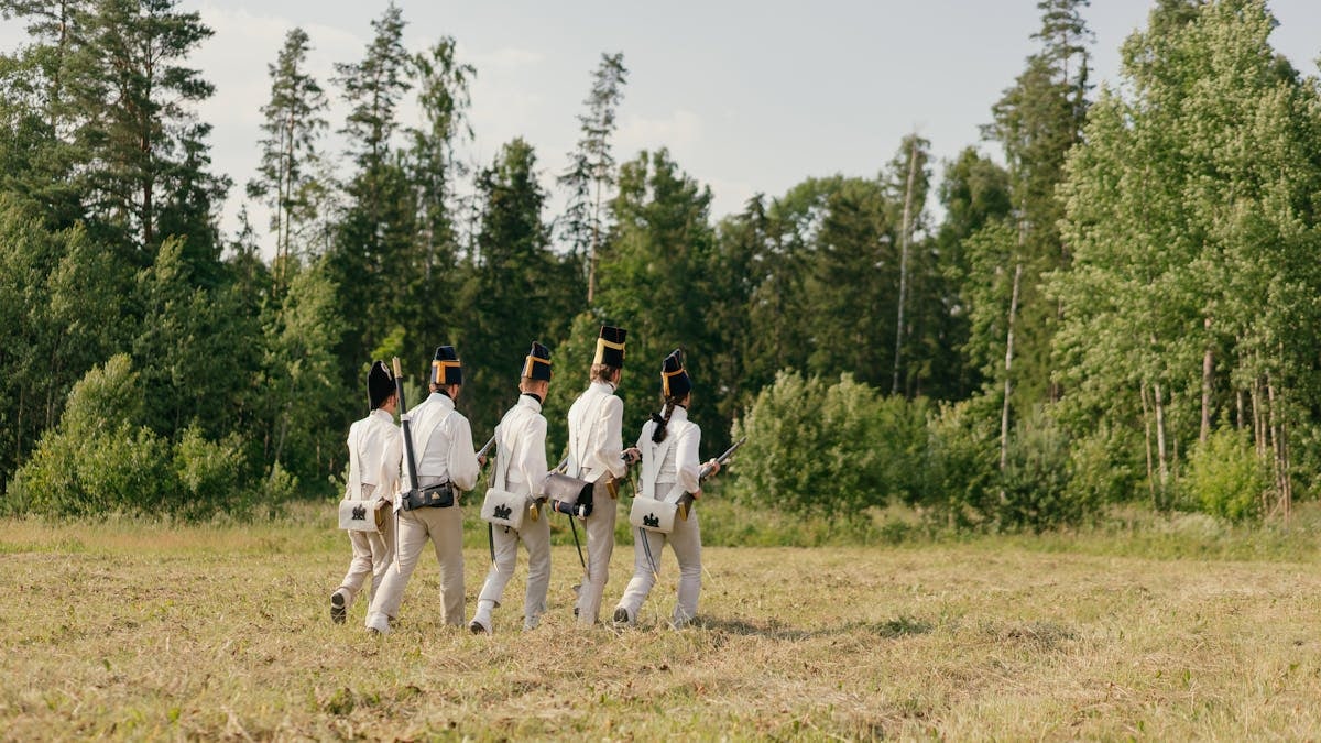 Group of soldiers in historical uniforms marching through a forest clearing.